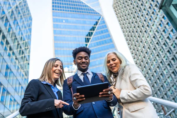 Çeşitli iş adamları gülümsüyor ve takım çalışması gösteriyor, kurumsal bir şehir ortamında birlikte tablete bakıp modern dijital stratejiyi tartışıyorlar.