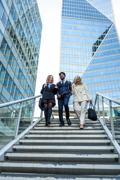 Modern bir finans bölgesinde işbirliği yapan ve merdivenlerden inen çeşitli iş adamları, takım çalışması, kentsel yaşam ve profesyonel ilerleme kavramlarını yansıtıyorlar.