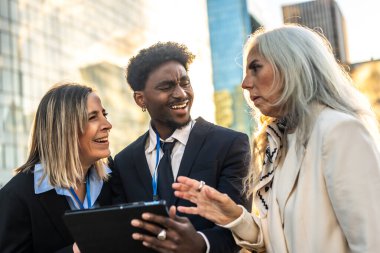 Çeşitli iş adamları, strateji, takım çalışması ve modern iş yeri iletişimi konularını tartışırken kentte bir tablet üzerinde gülümseyerek ve işbirliği yaparak bir araya geliyorlar.