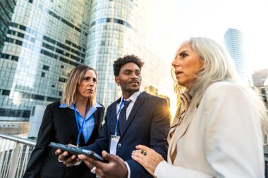 Çeşitli iş adamları açık havada toplantı yapıyor, iş birliği yapıyor ve tartışıyorlar, modern bir şehir kurumunda dijital tablet üzerindeki verileri analiz ediyorlar.