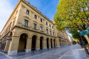 San Sebastian 'daki Gipuzkoa kare cephesi. Ağaç kaplı bir cadde boyunca tekrarlayan taş kemerler ve pencereler. Huzurlu bir şehir manzarası çerçeveleyen klasik dekoratif mimari.