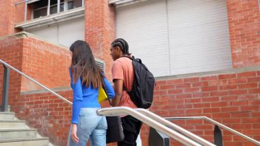 Sırt çantalı genç çok kültürlü arkadaşlar modern bir üniversite binasının merdivenlerinden birlikte sınıfa çıkıyorlar ve yoldaşlık ve öğrenci hayatı paylaşıyorlar.