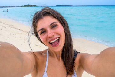 Beyaz bir maldivian plajında selfie için gülümseyen bir kadın, turkuaz okyanus, mavi gökyüzü ve kaygısız yaz neşesi ile güneşli tropik tatil titreşimlerini kucaklıyor.