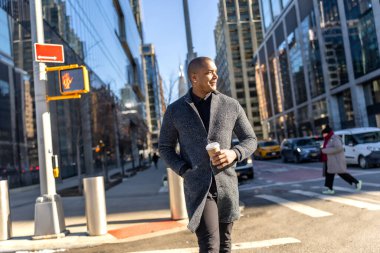 Şık ceketli genç adam elinde kahve tutarak Manhattan sokaklarında yürüyor, cam binalar arasında rahatça geziniyor modern şehir hayatı ve yoğun iş hayatı