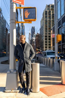 Manhattan caddesinde yaya geçidinde ayakta gülümseyen bir adam. Arka planda binalar ve trafik vardı. Yürüyüş sinyaliyle karşı karşıyaydı.
