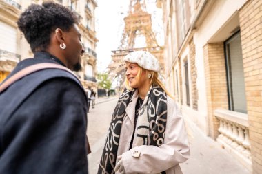 Arka planda Eyfel kulesi olan bir Paris caddesinde gülümseyen ve etkileşime giren mutlu çift, romantizmi, seyahati ve şehir keşiflerini simgeliyor.