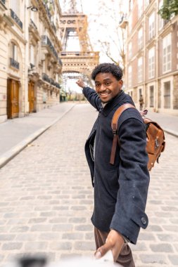 Mutlu siyah adam, birini kaldırım taşı sokağından aşağı indiriyor. Gülümsüyor ve Eyfel Kulesi 'ni işaret ediyor.