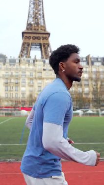 Çalışmaları sırasında kırmızı pistte koşan kararlı bir genç adamın yan görüntüsü. Arka planda Eyfel Kulesi var. Paris 'te aktif bir şehir yaşam tarzı sergiliyor.