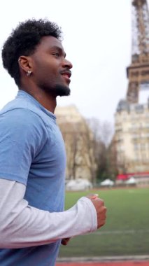 Atletik Afrikalı Amerikalı adam arka planda Eyfel Kulesi ile koşu pistinde koşuyor, Paris, Fransa 'da sağlıklı bir yaşam tarzı ve açık hava egzersizinin tadını çıkarıyor.