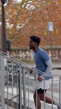 Spor giyimli Afro-Amerikan atletik genç bir adam kardiyo çalışması sırasında merdivenlerden yukarı koşuyor. Bir sonbahar günü, bir Avrupa kenti caddesinde azimli bir erkek koşucu eğitimi almak ve odaklanmak.