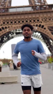 Atletik genç Afrikalı Amerikalı adam Paris 'te açık havada koşuyor, sabah koşusunun tadını çıkarıyor ve arka planda ikonik Eyfel kulesi ile sağlıklı ve aktif bir yaşam tarzı sürdürüyor.