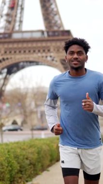 Paris, Fransa 'da bir parkta koşan afro saçlı genç atletik bir adam, günlük çalışma rutini için, bulutlu bir günde arka planda ikonik Eyfel kulesi görünür.