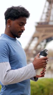 Genç atletik Afrikalı Amerikalı adam, arka plandaki Eyfel kulesiyle yaptığı çalışmadan sonra tekrar kullanılabilir bir şişeden su içiyor ve aktif ve sağlıklı bir yaşam tarzını destekliyor.
