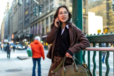 Manhattan 'da genç bir iş kadını akıllı bir telefonla yürüyor ve konuşuyor, şık giyinmiş, kentsel iş hayatını aktarıyor, bağlantı, güven ve şehirde odaklanmış aktivite