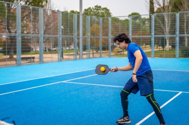 Spor giyim sektöründe genç bir adam, açık hava mavi kortunda raketle bir yankesiciye vuruyor. Rekabetçi oyun kondisyonu ve aktif yaşam tarzı sırasında odaklanmış ve enerjik.