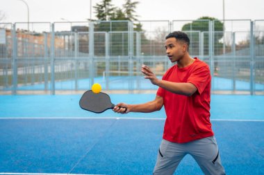 Pickleball maçında, açık hava sahasında topu iade etmeye odaklanan genç adam sağlıklı, aktif bir yaşam tarzına ve eğlence amaçlı bir spora girişiyor.