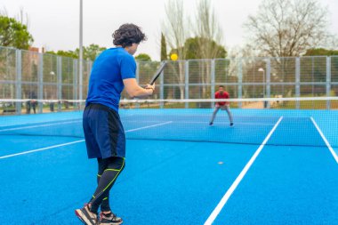 İki genç adam canlı bir mavi sahada, canlı bir penisbol oyununa girişiyor. Ağ üzerindeki sarı topa raketleriyle vurmaya odaklanıyor.