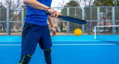 Atletin sarı bir picleball 'a raketle vurması canlı bir mavi sahada, ralli ortasında gündelik yarışma sırasında odak, güç ve yaz fitness gösterisi.