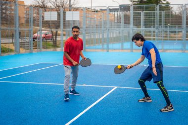 İki adam, dinamik ve enerjik bir maçta raket ve topla bir araya geldiklerinde odaklanmış ve atletik bir şekilde, açık hava sahasında Pickleball 'da yoğun bir şekilde yarışıyorlar.