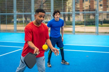 Pickleball oynayan, aktif olarak eğlenen ve açık hava spor sahasından zevk alan, modern bir yarışma aktivitesinde beceri ve takım çalışması geliştiren genç erkekler.