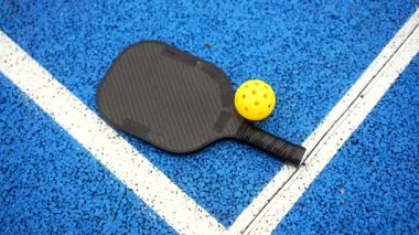 Sarı yankesicilik ve karbon fiber kürek canlı bir mavi sahanın beyaz çizgilerinde duruyor. Bu, tenis ve badminton unsurlarını birleştiren her yaş için popüler ve hızlı büyüyen bir sporu temsil ediyor.