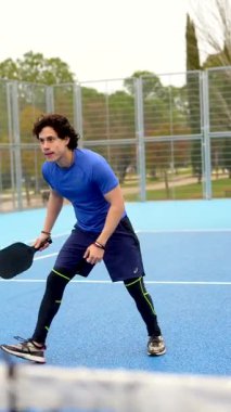 Yoğunlaşmış genç bir adam, canlı bir mavi sahada oynanan ve galibiyet puanını kutlamadan önce yoğun bir odak ve atletik beceri gösteren bir yarışma sırasında raketle raketlere vuruyor.