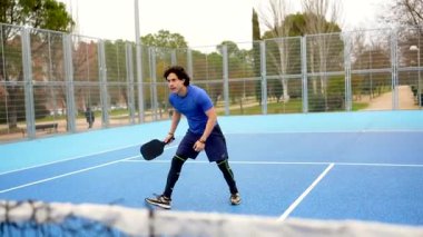 Spor giyim sektöründe atletizm antrenmanı yapan atletik bir adam, açık hava antrenmanı sırasında mavi kortta raketle sarı bir topa vuruyor, yetenek, güç ve konsantrasyon gösteriyor.