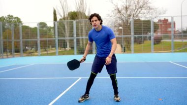 Modern bir mavi kortta, atletik bir adam topa ustalıkla vurarak, odaklandığını ve çevikliğini gösteren enerjik bir açık hava maçı sırasında topa vuruyor.