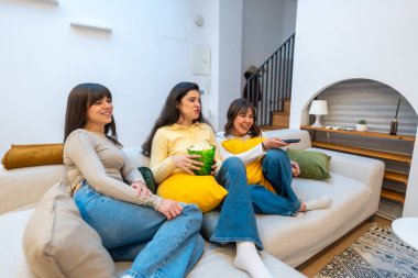 Bir grup mutlu genç bayan arkadaş evdeki rahat bir kanepede dinleniyor, birlikte vakit geçiriyorlar, patlamış mısırla sıcak bir film gecesi boyunca gülüyor ve televizyon izliyorlar.