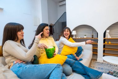 Üç kadın kanepede patlamış mısır paylaşıyor, rahat bir oturma odasında gülüyor ve televizyon seyrediyor, evde rahat bir film gecesi ve gündelik bir arkadaşlığın tadını çıkarıyor.