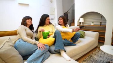 Evde rahat bir koltukta oturan, patlamış mısır yiyip uzaktan kumandayla kanal değiştiren üç genç kız arkadaştan oluşan bir grup.