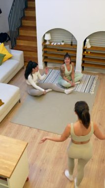 Modern bir oturma odasındaki halının üzerinde oturan üç mutlu bayan arkadaş antrenmandan sonra gülüp, birlikte portakallarla hokkabazlık yapıyorlar. Evlerinde neşe ve dostluk anları sergiliyorlar.