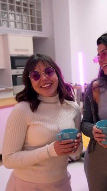 Üç neşeli genç bayan, sıcak bir oturma odasında gülüp sohbet ediyorlar. Zarif bayan arkadaşlar rahat bir ev partisi sırasında sıcak içeceklerle bardakları tutarken arkadaşça sohbetin tadını çıkarıyorlar.