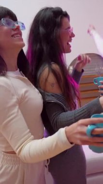 Neşeli bayan arkadaşlar renkli güneş gözlüğü takıyor dans ediyor, şarkı söylüyor ve birlikte eğleniyorlar sıcak içeceklerin keyfini çıkarırken canlı mor neon ışıklarla dolu bir ev partisinde