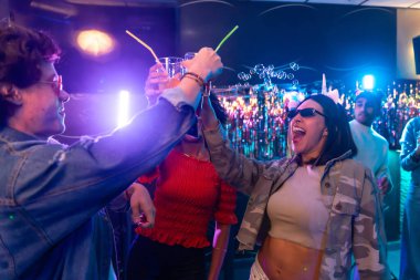 Çeşitli yetişkin arkadaşlar parlayan pipetlerle kokteyller içiyor, renkli ışıklar ve kabarcıklarla çevrili neşeli bir geceyi kutluyor ve eğleniyorlar.