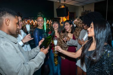 Genç bir grup arkadaş bir gece kulübünde özel bir olayı kutluyorlar, bardaklara şampanya dolduruyorlar ve kadeh kaldırıyorlar, parti atmosferinin tadını çıkarıyorlar.