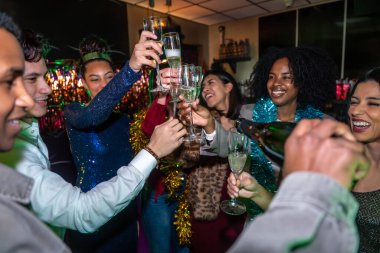 Bir grup farklı arkadaş bir aradayken, şampanya kadehleriyle gülümsüyor ve kadeh kaldırırken şenlikli, loş bir mekanda özel bir kutlama yapıyorlar.