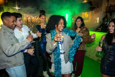 Bir grup genç yetişkin, neşeli bir gece kulübünde ya da barda şampanya bardakları tutarken eğleniyor, dans ediyor ve gülüyor. Özel bir olayı kutlama ışıklarıyla ve dumanla kutluyorlar.