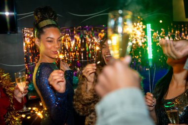 Bir grup farklı arkadaş birlikte kutlama yapıyor, neşeli bir gece hayatı etkinliği sırasında ellerinde maytap ve şampanya bardaklarıyla, canlı atmosferin tadını çıkarıyorlar.