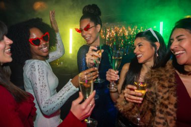 Bir grup gülümseyen genç kadın canlı bir gece kulübünde şampanyayla kadeh kaldırıyor. Renkli ışıklarla, dansla ve neşe dolu birlikteliğimizle özel bir olayı kutluyorlar.