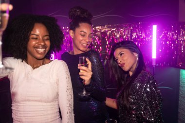 Üç farklı kadın arkadaş geceyi dışarıda geçiriyorlar, şampanyayla kadeh kaldırıyorlar ve canlı bir gece kulübünde mor neon ışıklarla kutlama yapıyorlar.