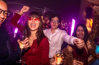 Çeşitli genç arkadaşlar dans ediyor ve tezahürat yapıyorlar, ellerinde alkollü içkiler bardaklarıyla, heyecan verici mor neon ışıkları ve canlı bir atmosferi olan canlı bir gece hayatı partisinin tadını çıkarıyorlar.