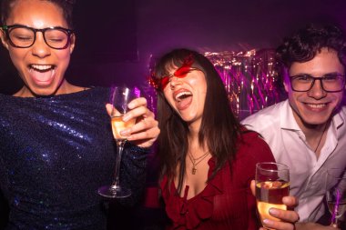 Mor kulüp ışıkları altında gülen ve şampanya içen mutlu genç arkadaşlar, neşeli, çeşitli gece hayatı sahnelerinde birlikte kutlama yapıyorlar, neşe, neşe ve güzel zamanlar.