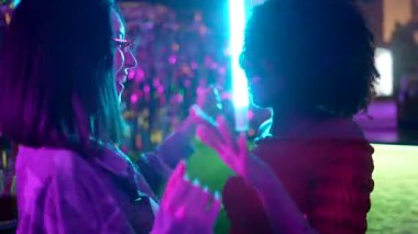 Neşeli, çeşitli, güneş gözlüklü bayan arkadaşlar. Canlı mavi ve mor neon ışıkları olan bir gece kulübündeki partide birlikte gülüp dans ediyorlar. Müzikten ve canlı atmosferden keyif alıyorlar.