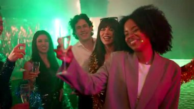 Dans eden, gülümseyen ve bir gece kulübünde şampanya kadehleriyle kadeh kaldıran neşeli atmosferin tadını çıkaran ve renkli ışıklarla kutlayan çok kültürlü genç arkadaşlar grubu.