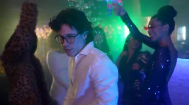 Gözlüklü genç adam renkli neon ışıkları olan bir gece kulübü partisinde arkadaşlarıyla dans ediyor. Enerjik kalabalık müzik dinliyor ve dans pistinde sabun köpükleri uçuşurken kutlama yapıyor.