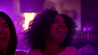 Mutlu bir grup arkadaş dans ediyor, şampanya içiyor ve renkli mor neon ışıkları ve kutlama atmosferi olan kalabalık bir gece kulübünde eğleniyor.