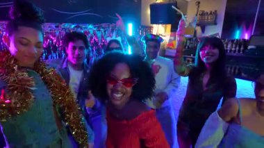 Neşeli çoklu etnik arkadaş grubu birlikte dans ediyor, gülümsüyor ve neon ışıklı bir gece kulübünde eğleniyor, gece hayatını müzik ve içkilerle kutluyor ve eğleniyorlar.