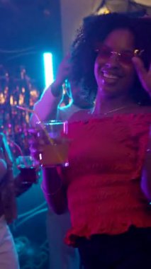 Afro saçlı genç Afrikalı Amerikalı bir kadın elinde bir gece kulübü partisinde elinde bir kokteyl ile gülüyor ve dans ediyor. Gece hayatının müziğinin ve neon ışıklarının keyfini çıkarıyor.