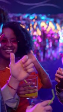 Kalabalık bir dans pistinde dans eden, kokteyl içen, neon ışıklı ve uçan baloncuklu mutlu genç arkadaşlar, müzik ve eğlence ile eğlenceli bir gece geçiriyorlar.